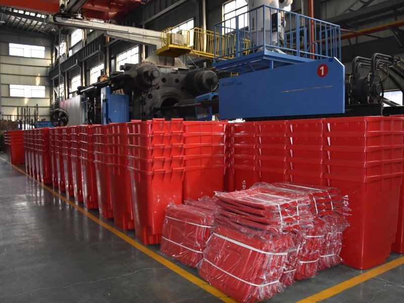 Red plastic waste bin are stacked together in the factory,with packaged waste bin lids next to them