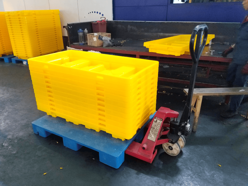 Stacked yellow spill trays on plastic pallet, ready for shipment in production area